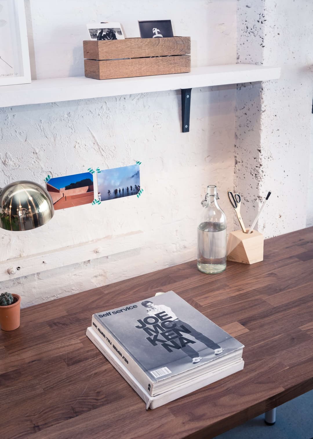 A quiet desk corner in the workroom, with a walnut desk and shelving against white brick